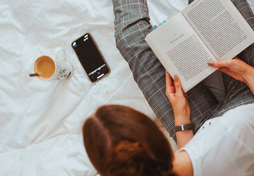 Girl in bed reading with phone beside her